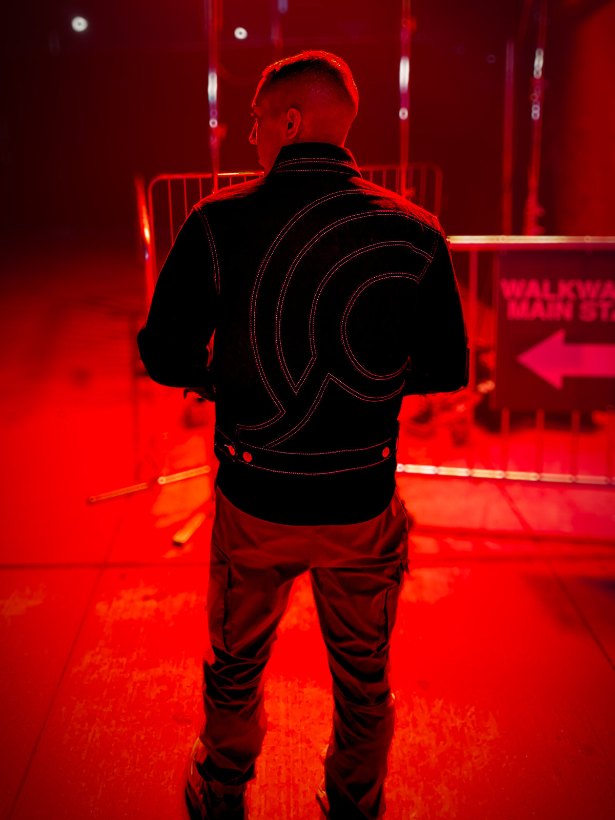 Rear view of a person at a concert in New York at night wearing the black Midnight Voyager denim jacket with signature curved contrast stitching.