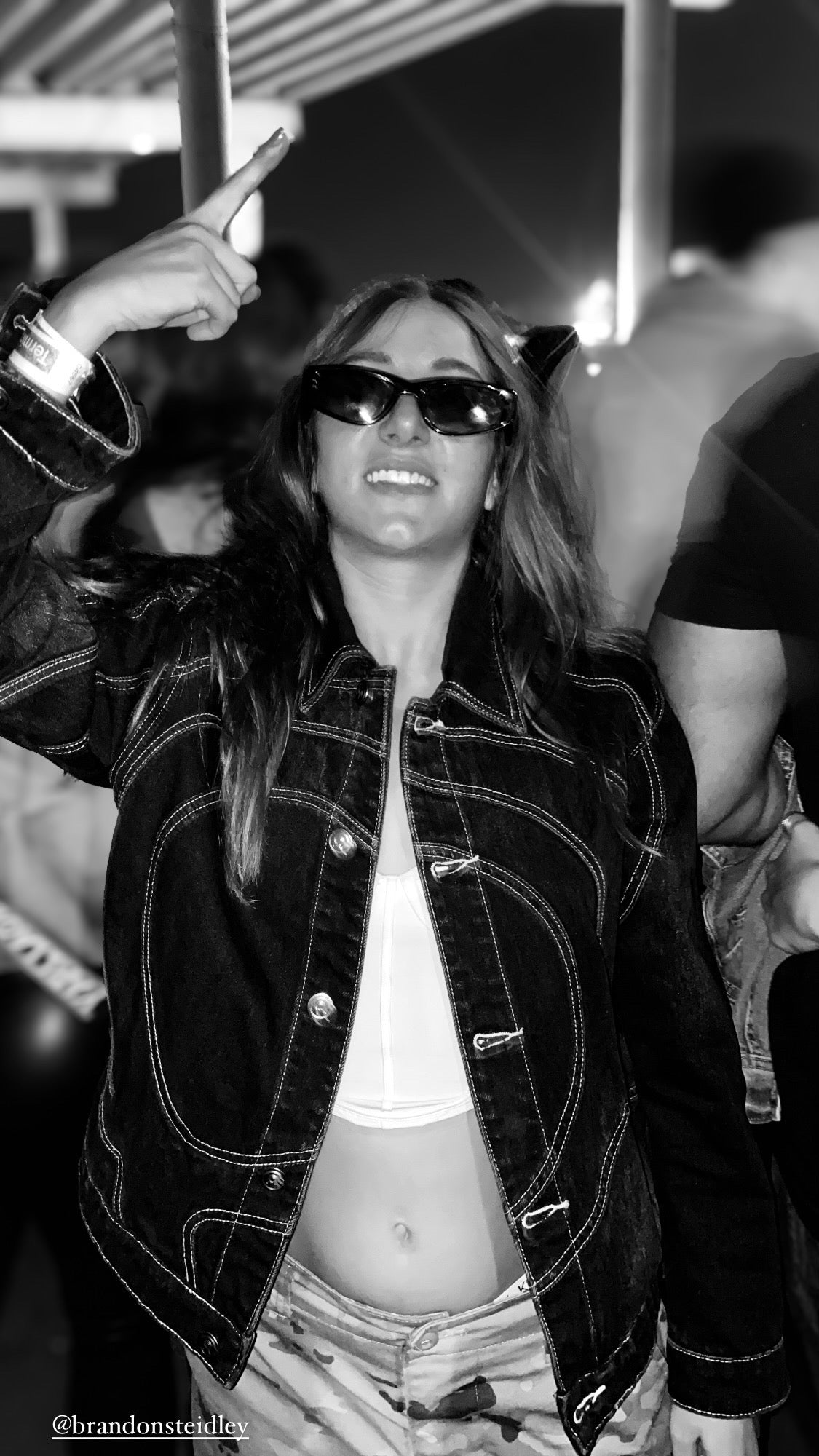 Person wearing the black Midnight Voyager denim jacket with signature curved contrast stitching and sunglasses at a Black Coffee concert.