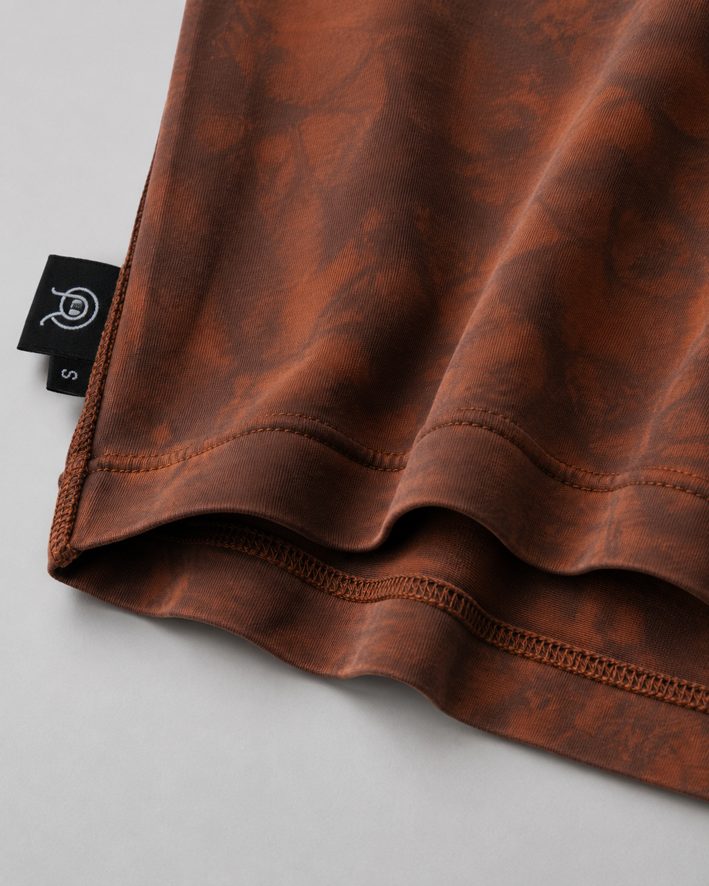 Close-up of the exposed overlock seam construction on the reversible Sunfaded T-Shirt. showing the texture and a black product tag with a white logo.